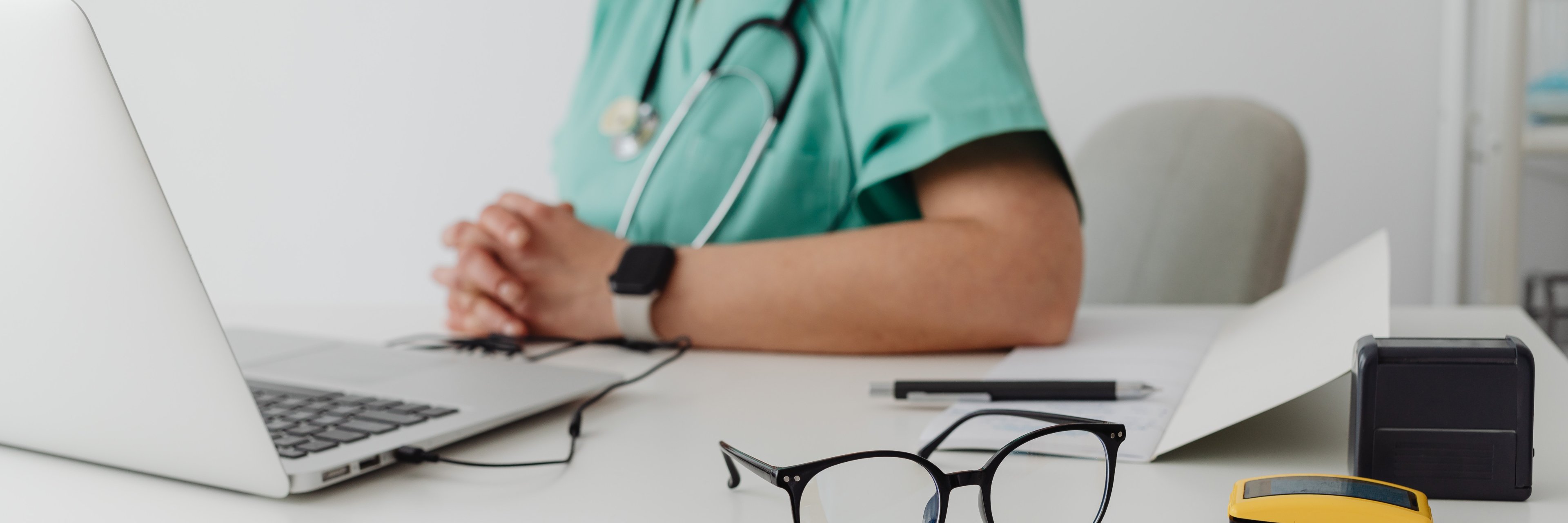 Ärztin sitzt vor einem Schreibtisch mit Laptop und Brille